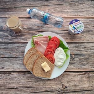 Zdjęcie przedstawia Dietę z ograniczeniem łatwoprzyswajalnych węglowodanów Masło extra Kawa zbożowa z mlekiem Chleb Graham Szynka Piastowska Jogurt naturalny Woda mineralna Sałata zielona Pasta z twarogu z natką pietruszki Pomidor